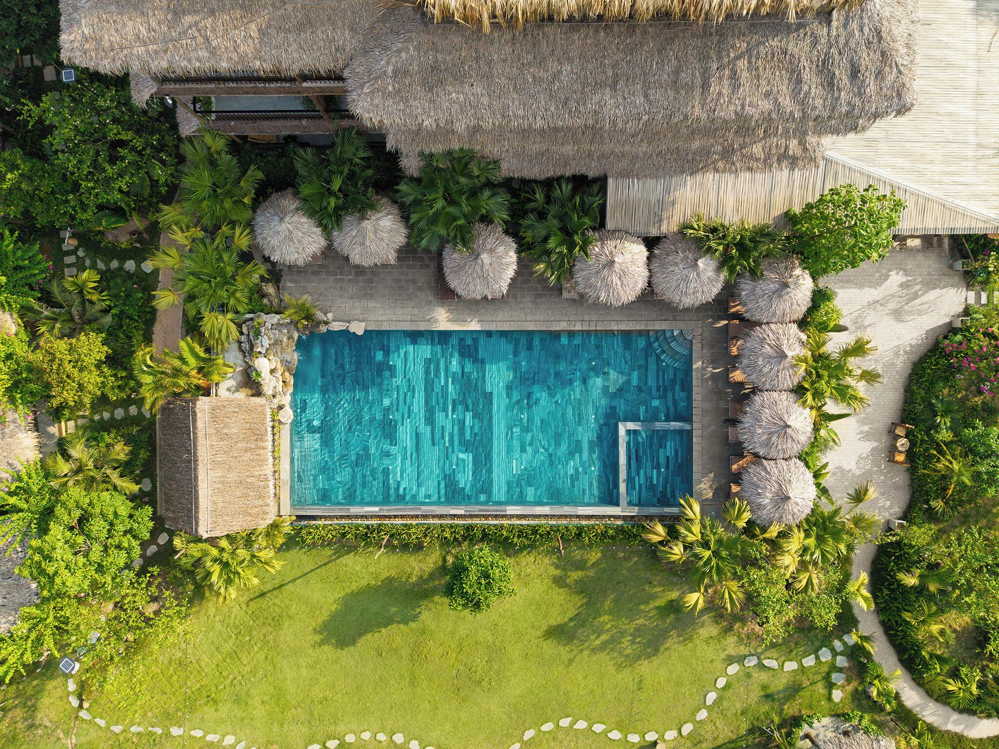 An aerial view of a swimming pool surrounded by lush greenery and thatched structures.