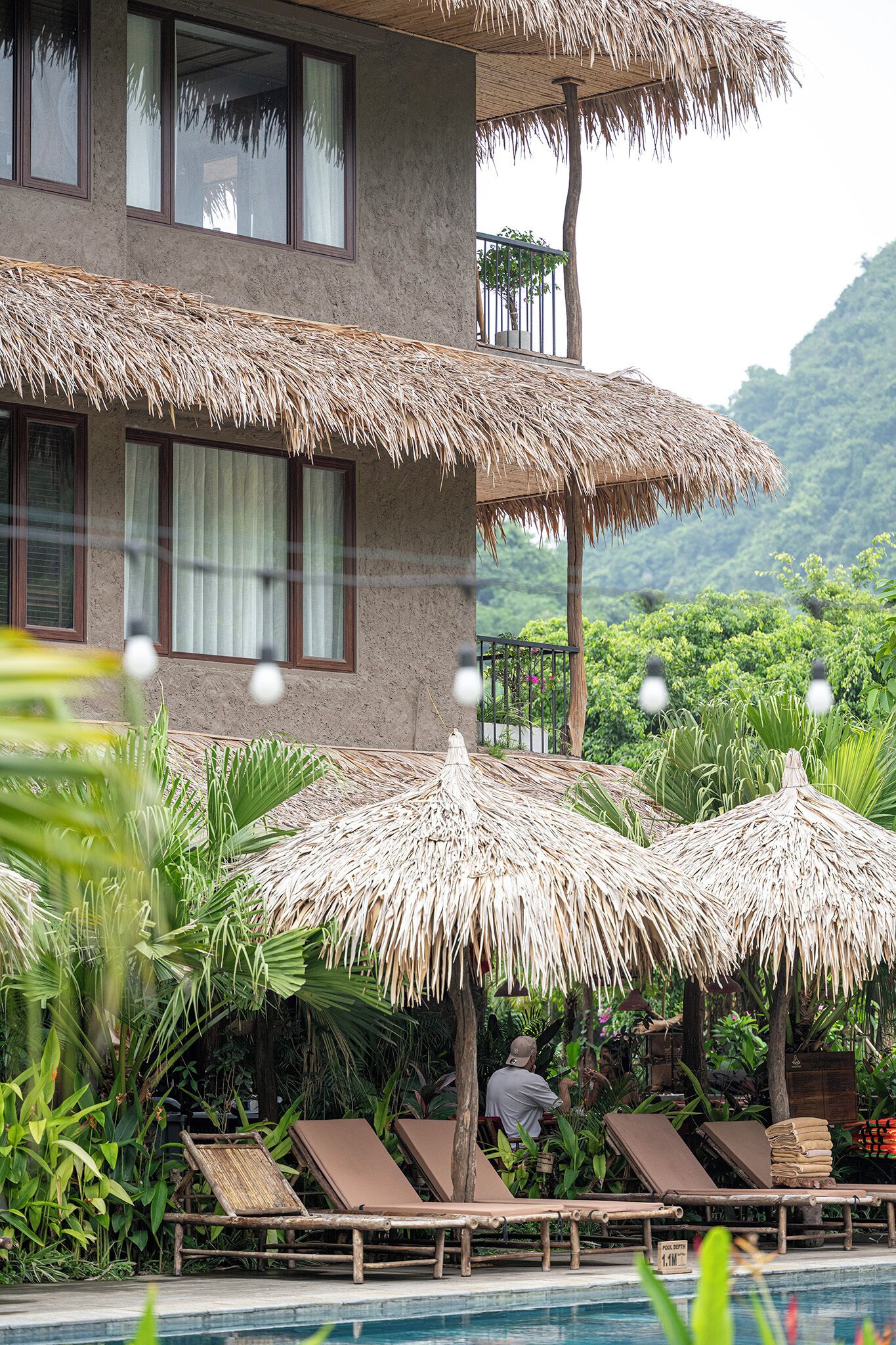 A hotel with a pool area, thatched umbrellas, and lounge chairs.