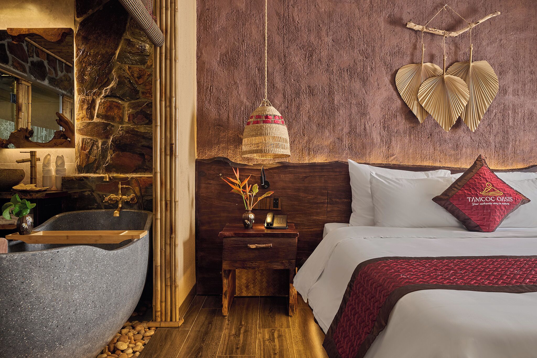 Una habitación con un lavamanos de piedra, una mesita de noche de madera con una lámpara, una cama con un cojín rojo y una pared con una decoración con forma de corazón.