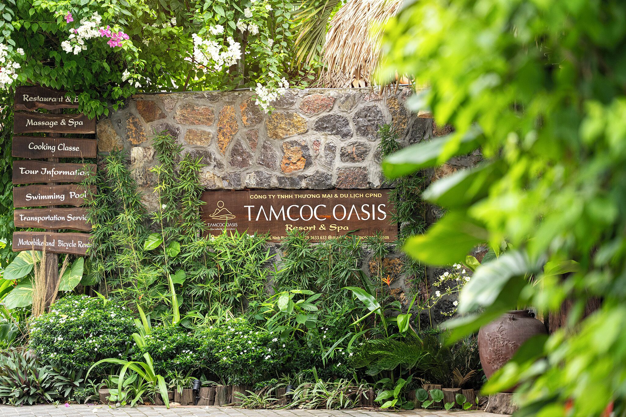 A stone wall with signs for a restaurant, massage spa, cooking class, information, swimming pool, transportation service, and rental bikes.