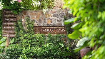 A stone wall with signs for a restaurant, massage spa, cooking class, information, swimming pool, transportation service, and rental bikes.