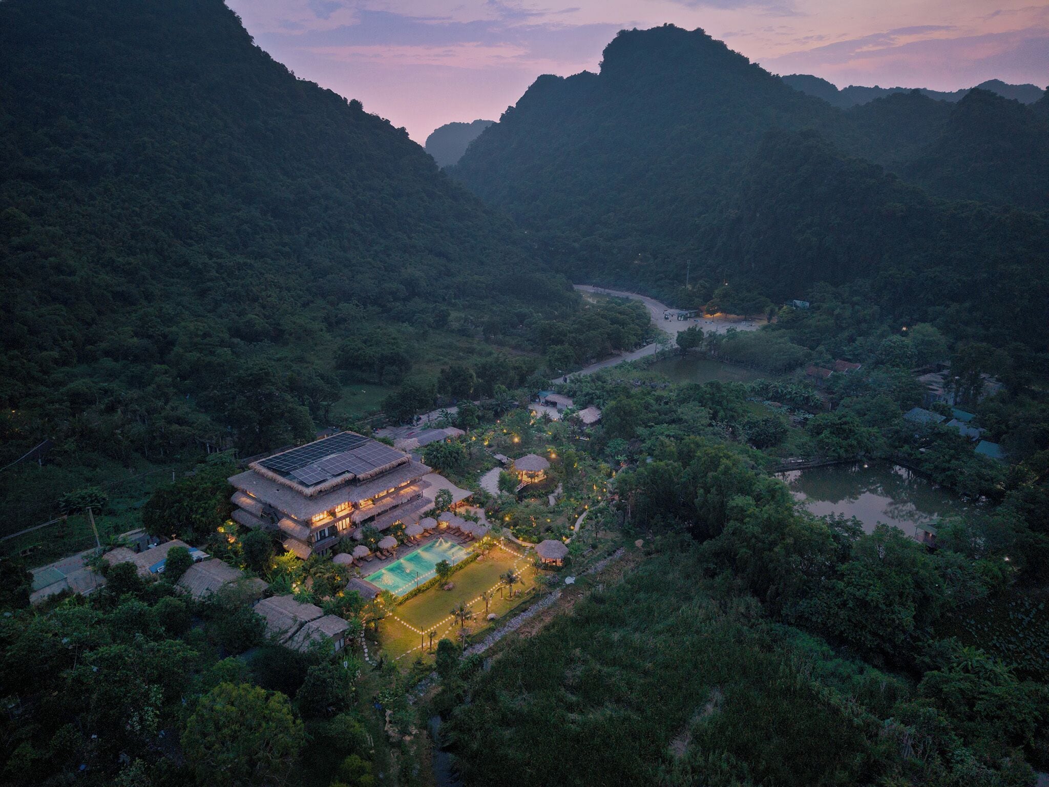 A resort with a swimming pool, thatched-roof buildings, and a view of a valley.
