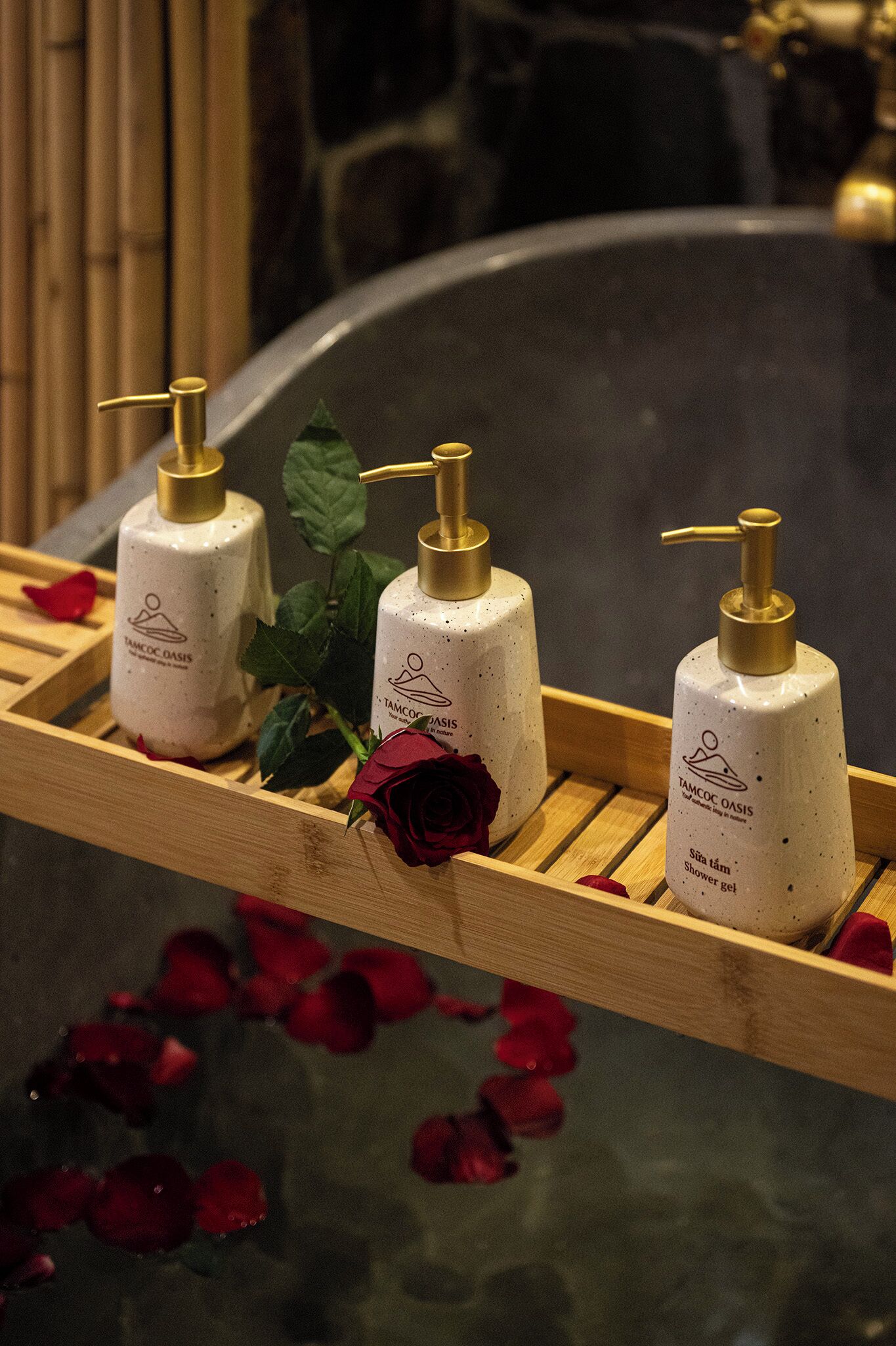Three bottles of Tamoc Oasis shower gel on a wooden tray with rose petals.