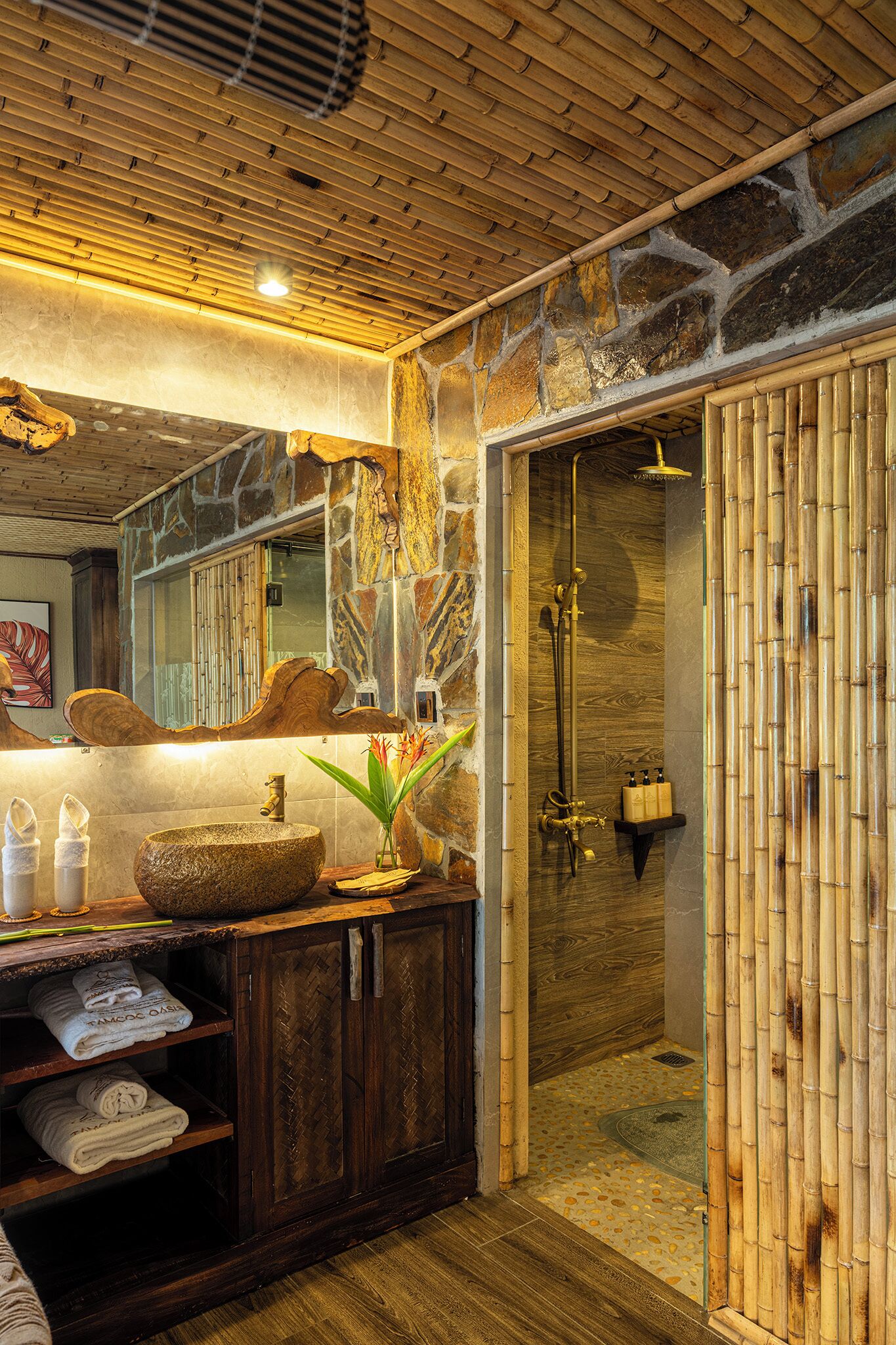 Une salle de bain avec un mur en pierre, un plafond en bois et une douche entourée de panneaux en bambou.