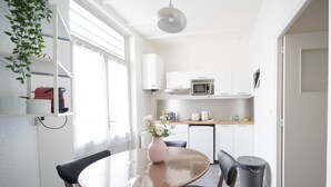 A modern kitchen with white cabinets, a microwave, and a coffee maker. There is a dining table with chairs and a vase of flowers.
