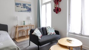 A modern living room with a sofa, a small table, a desk, and a window with curtains.
