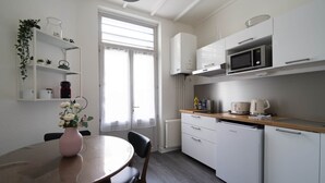 A modern kitchen with white cabinets, a microwave, and a coffee maker. There is a dining table with chairs and a vase of flowers.