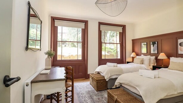 A bedroom with two beds, a desk, and a chair. There are two windows and a ceiling light fixture. - Grosvenor Abode, Royal Tunbridge Wells (Royal Tunbridge Wells)