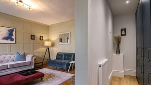 A modern living room with a sofa, armchair, and a red ottoman. There is a floor lamp and a painting on the wall. - Grosvenor Abode, Royal Tunbridge Wells (Royal Tunbridge Wells)