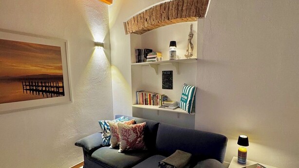 A cozy living room with a blue sofa, a small side table with a lamp, and a bookshelf with books and decorative items. - Accogliente appartamento nel centro storico a 1 minuto dal mare (Sestri Levante)