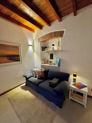 Un salon chaleureux avec un canapé bleu, une petite table d’appoint avec une lampe et une bibliothèque remplie de livres et d’objets décoratifs.