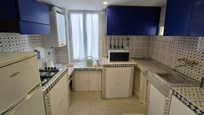 A compact kitchen with white cabinets, a refrigerator, a stove, and a microwave. There is a window with curtains, a sink, and a countertop with a kettle. - Accogliente appartamento nel centro storico a 1 minuto dal mare (Sestri Levante)