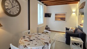 A cozy living room with a wooden ceiling, a round dining table with chairs, a sofa, a mounted TV, and a wall clock. - Accogliente appartamento nel centro storico a 1 minuto dal mare (Sestri Levante)