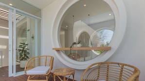 A room with a large round mirror, two wicker chairs with cushions, a small table, and a potted plant. - Villa Eudora 2br villa with private pool (Kec. Mengwi - Badung)