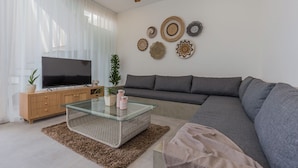 A modern living room with a flat-screen TV, a glass coffee table, a grey sofa, and decorative wall art. - Villa Eudora 2br villa with private pool (Kec. Mengwi - Badung)