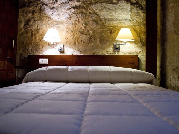 Un lit dans une chambre avec un mur en pierre et deux lampes fixées au mur.