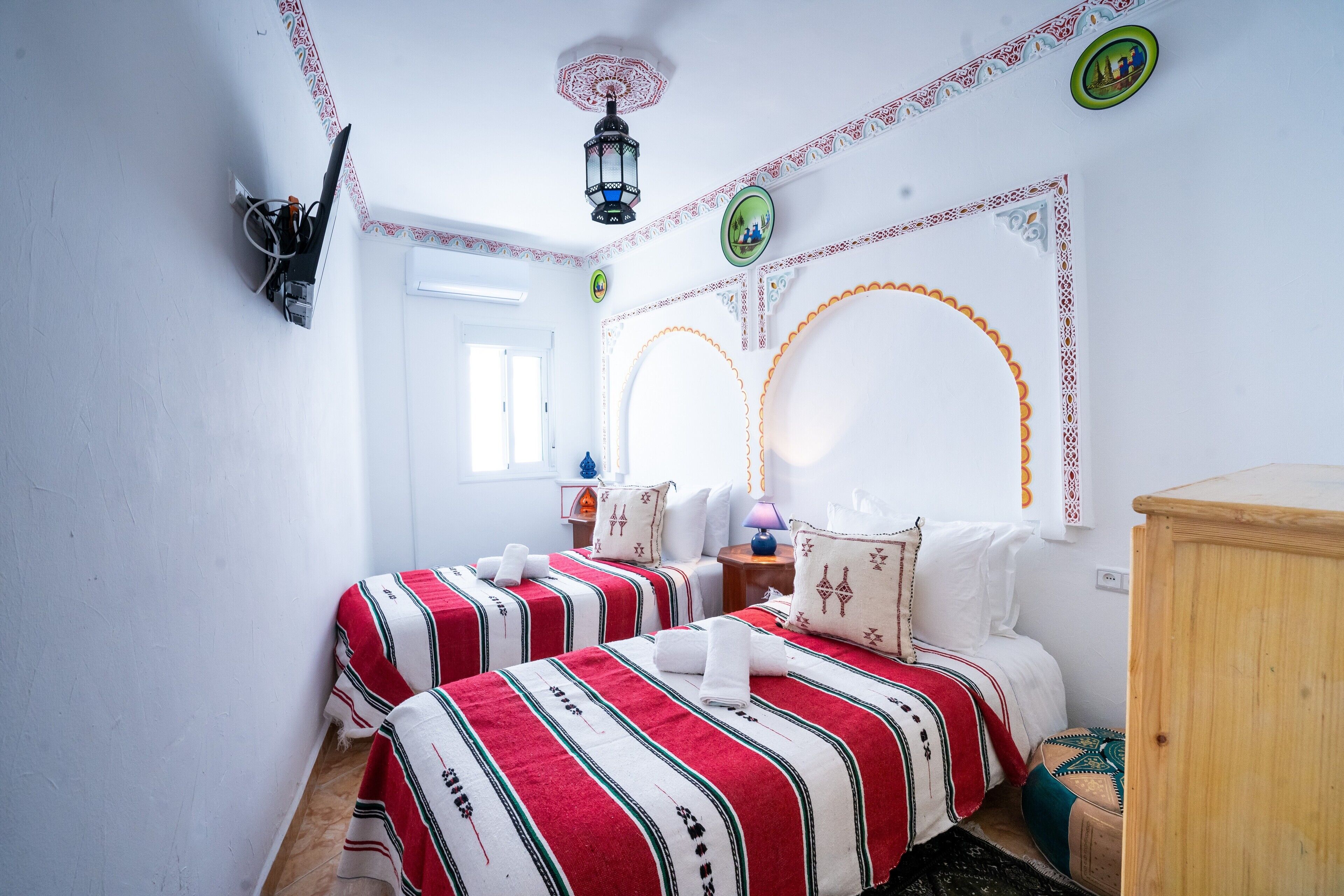 Une chambre avec deux lits, une armoire en bois, des motifs décoratifs sur les murs et un luminaire au plafond.
