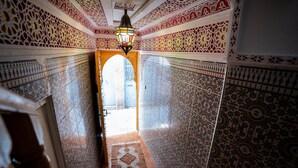 Un pasillo con elaborados diseños de azulejos y una puerta de madera que da a un espacio exterior.