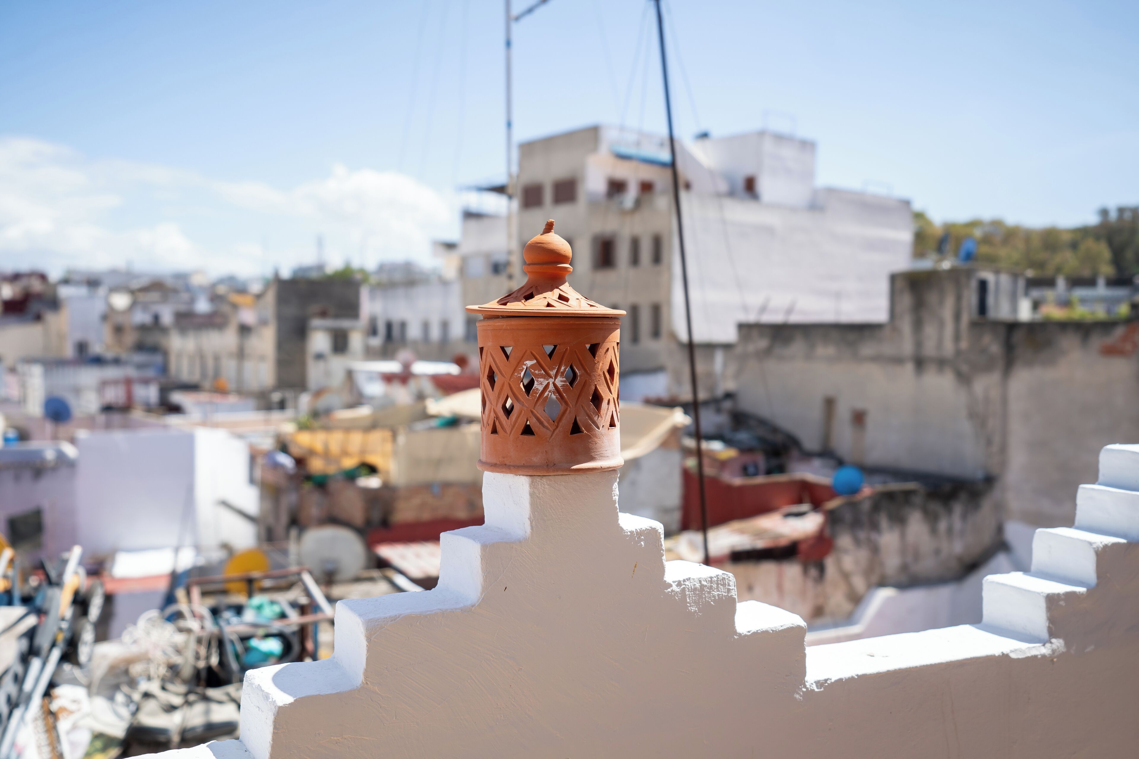A terracotta lantern atop a white wall, with a cityscape in the background.