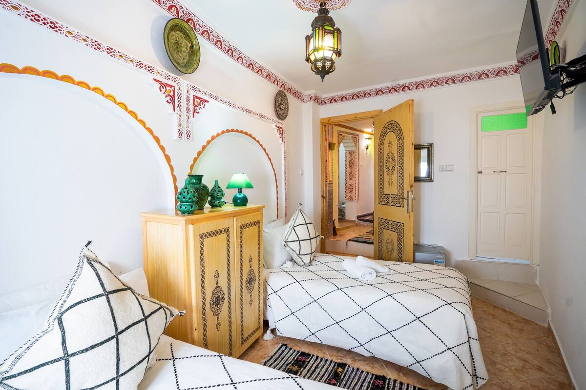 A bedroom with a bed, a wooden cabinet, decorative wall patterns, and a door leading to another room.