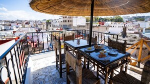 Una terraza con mesa lista para comer, sillas de mimbre y un paraguas de paja.