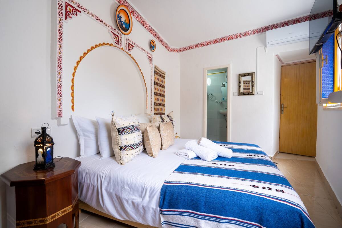 A bedroom with a bed, pillows, a nightstand, and a wall decoration.
