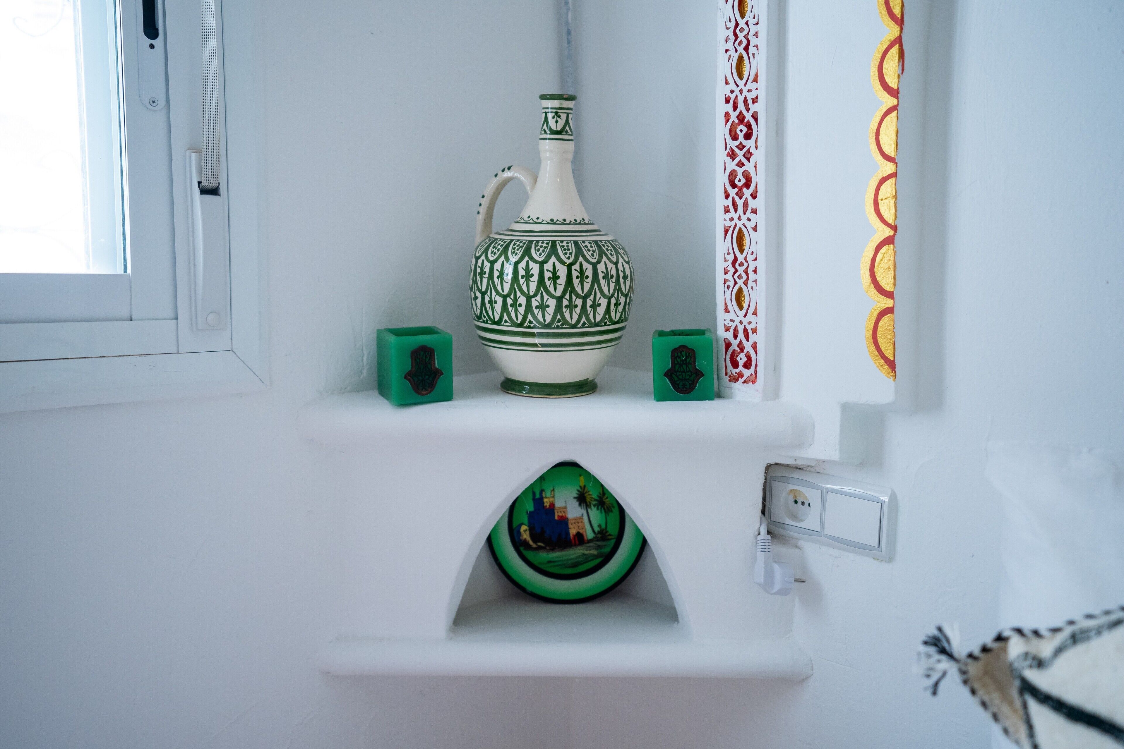 Een wit schap met een decoratieve groene en witte keramieken kruik, een groen en wit bord, en een klein groen doosje.