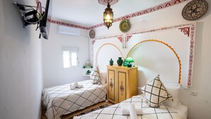 Un dormitorio con dos camas, un armario, diseños decorativos en la pared y una lámpara de techo.