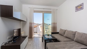 A modern apartment with a balcony, a sofa, a small table, and a TV.