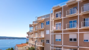 A multi-story building with balconies, a clear view of the sea, and a distant shoreline.