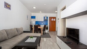 Una sala de estar con sofá, mesa de centro, televisor y una zona de cocina con armarios y mesa de comedor.