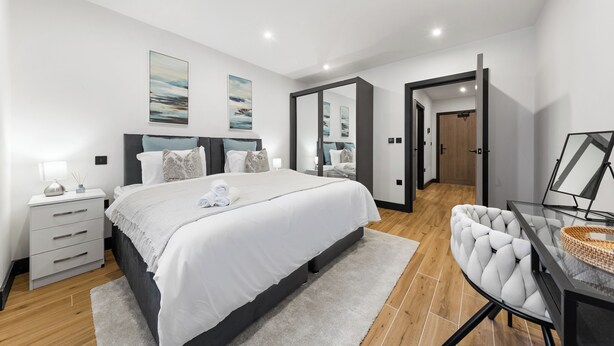 A modern bedroom with a large bed, bedside tables, a desk, and a chair. - Luxury 1 Bedroom Flat with private patio Sleeps 4 (London)