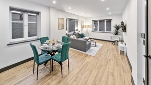 A modern living room with a dining area, large windows, and a grey sofa. - Luxury 1 Bedroom Flat with private patio Sleeps 4 (London)