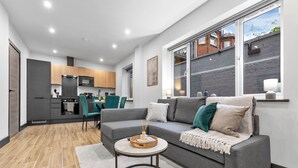 A modern living room with a grey sofa, a round coffee table, and a kitchen in the background. - Luxury 1 Bedroom Flat with private patio Sleeps 4 (London)