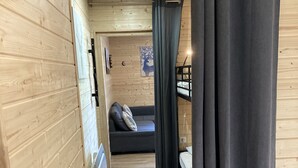 Ein Holzinnenraum mit einem Etagenbett, einer Couch mit Kissen, einer Wandheizung und einer Tür mit Griff.