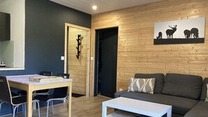 Ein modernes Wohnzimmer mit Holzwand, einem grauen Sofa, einem weißen Couchtisch und einem Essbereich mit Holztisch und Stühlen.