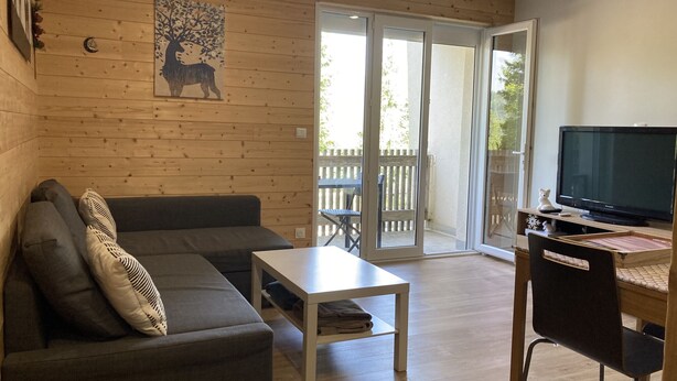 Ein gemütliches Wohnzimmer mit einer grauen Couch, einem kleinen weißen Tisch und einem Fernseher auf einem Holzständer.