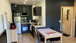 Eine kompakte Küche mit Mikrowelle, Herd und Spüle. Ein Esstisch mit Stühlen und ein kleiner Holzschrank sind vorhanden.