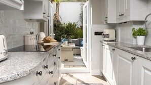 Een moderne keuken met witte kasten, granieten aanrechtbladen en uitzicht op een tuin via een open deur.
