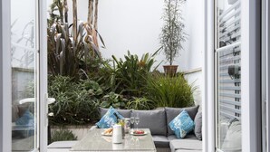 Een terras met een rieten tafel, kussens en een plant in pot.
