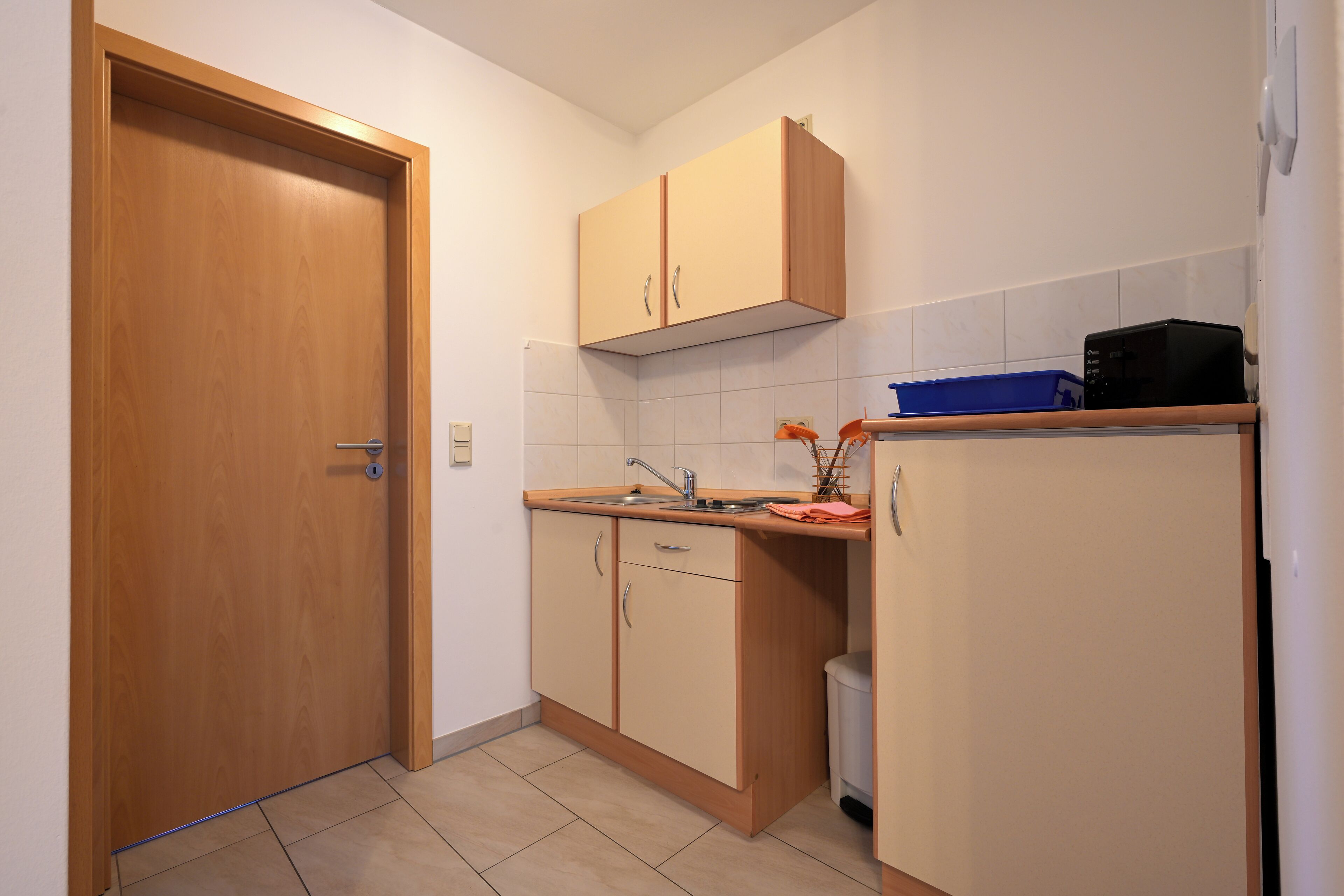 Een kleine keuken met houten kastjes, een spoelbak en een magnetron.