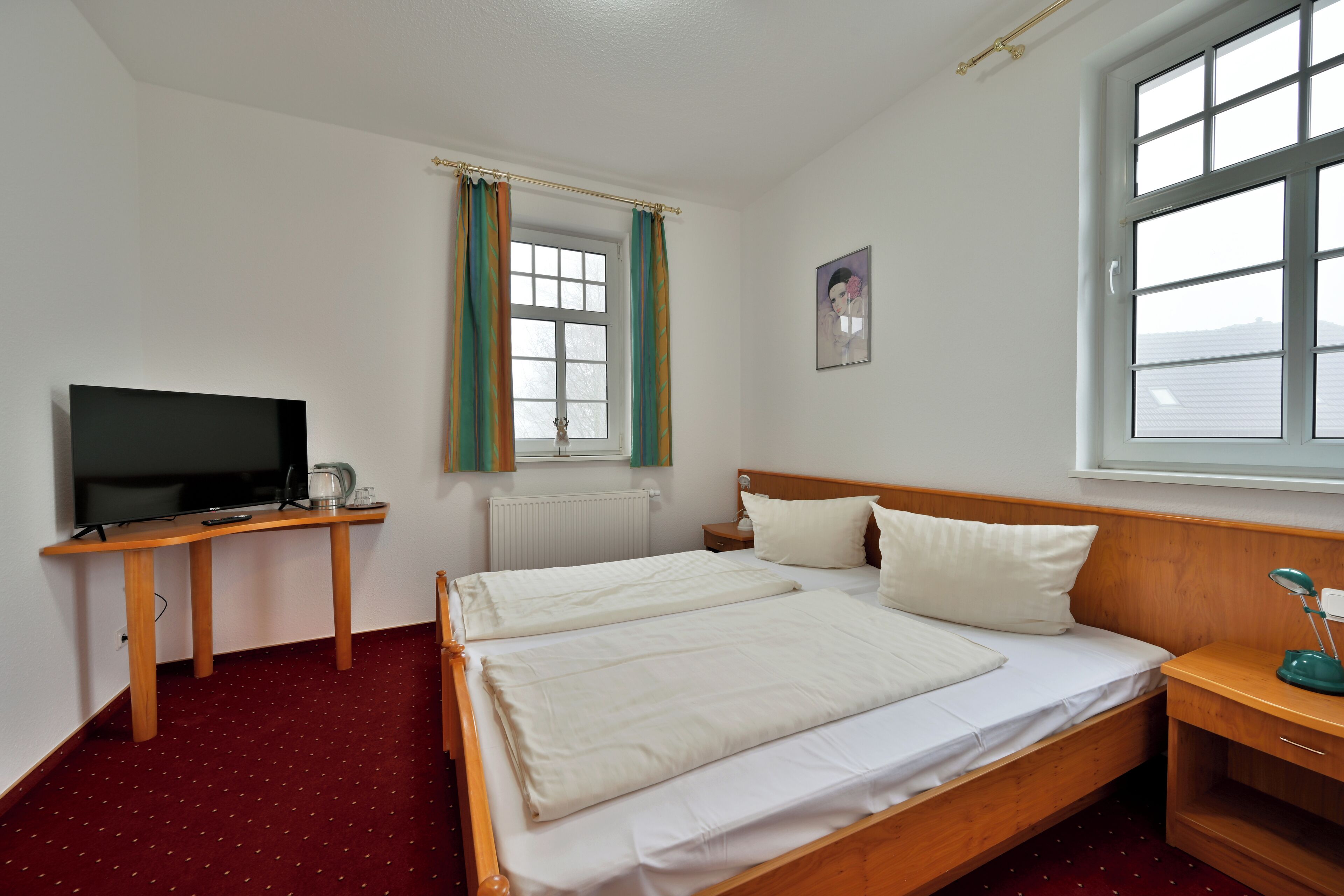 A bedroom with two beds, a TV, a desk, and a window.