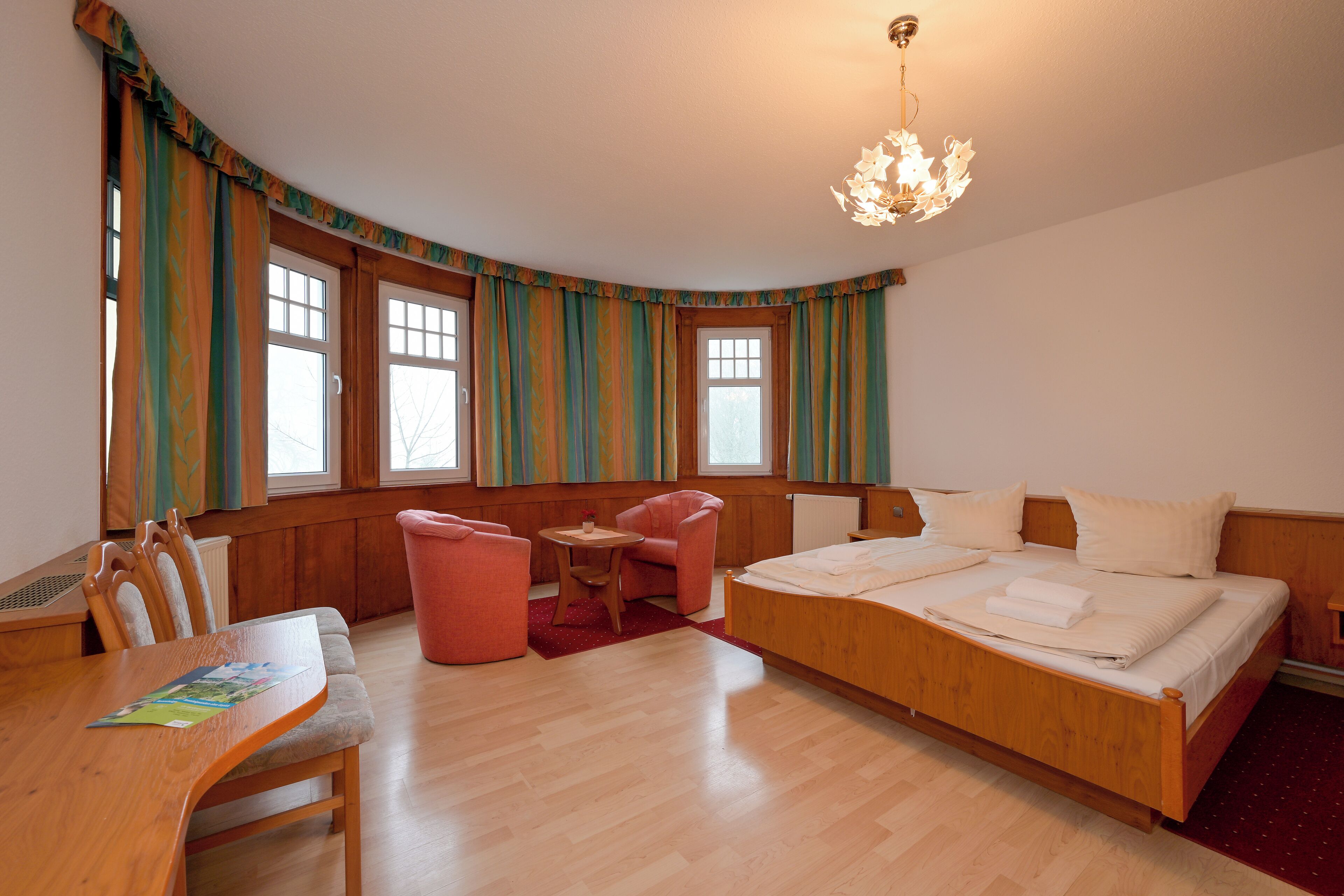 A bedroom with a wooden bed, a desk, a chair, and a small table.