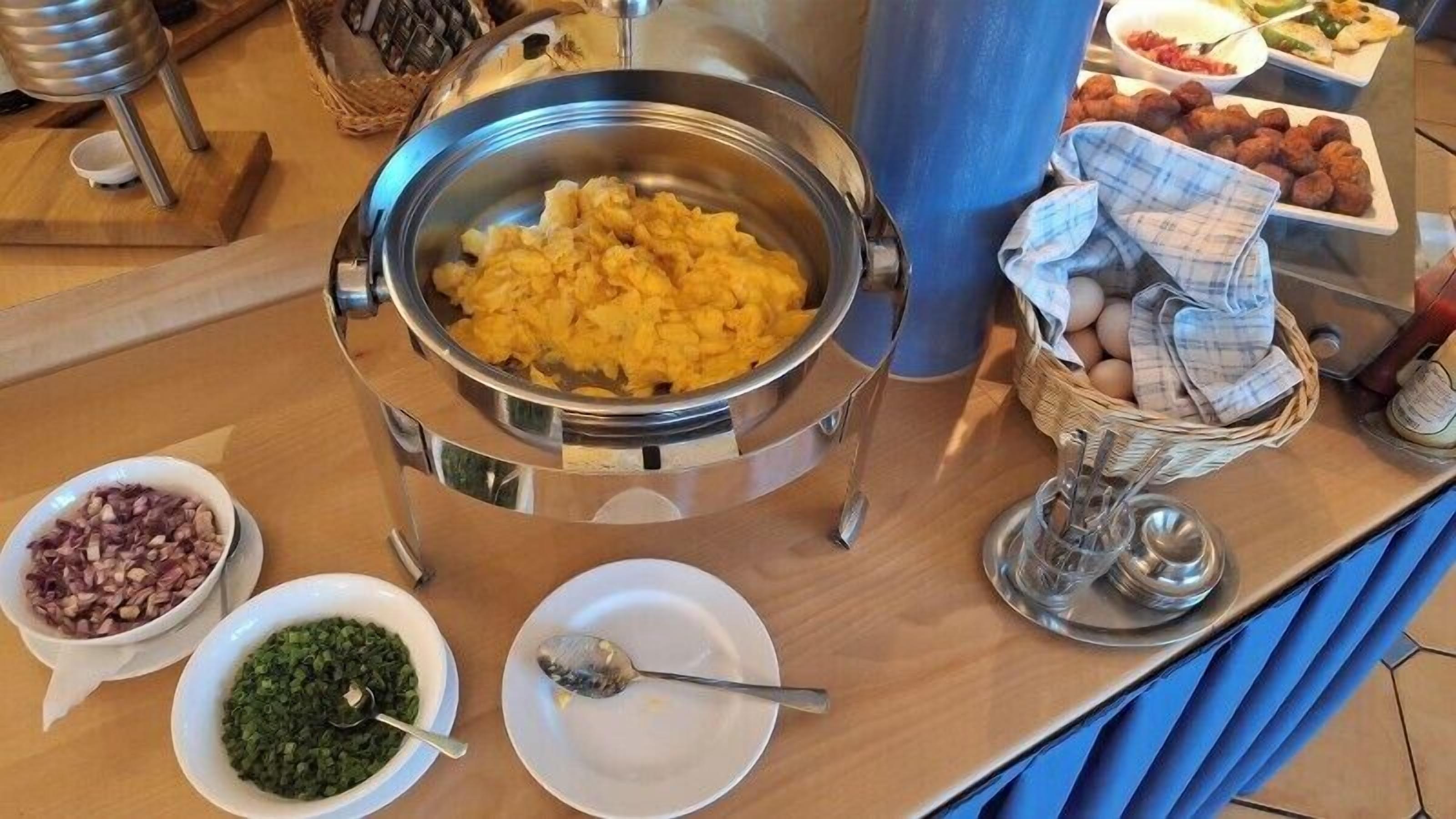 A buffet setup with various food items including scrambled eggs, chopped onions, and green vegetables.