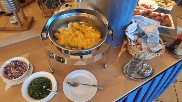 A buffet setup with various food items including scrambled eggs, chopped onions, and green vegetables.
