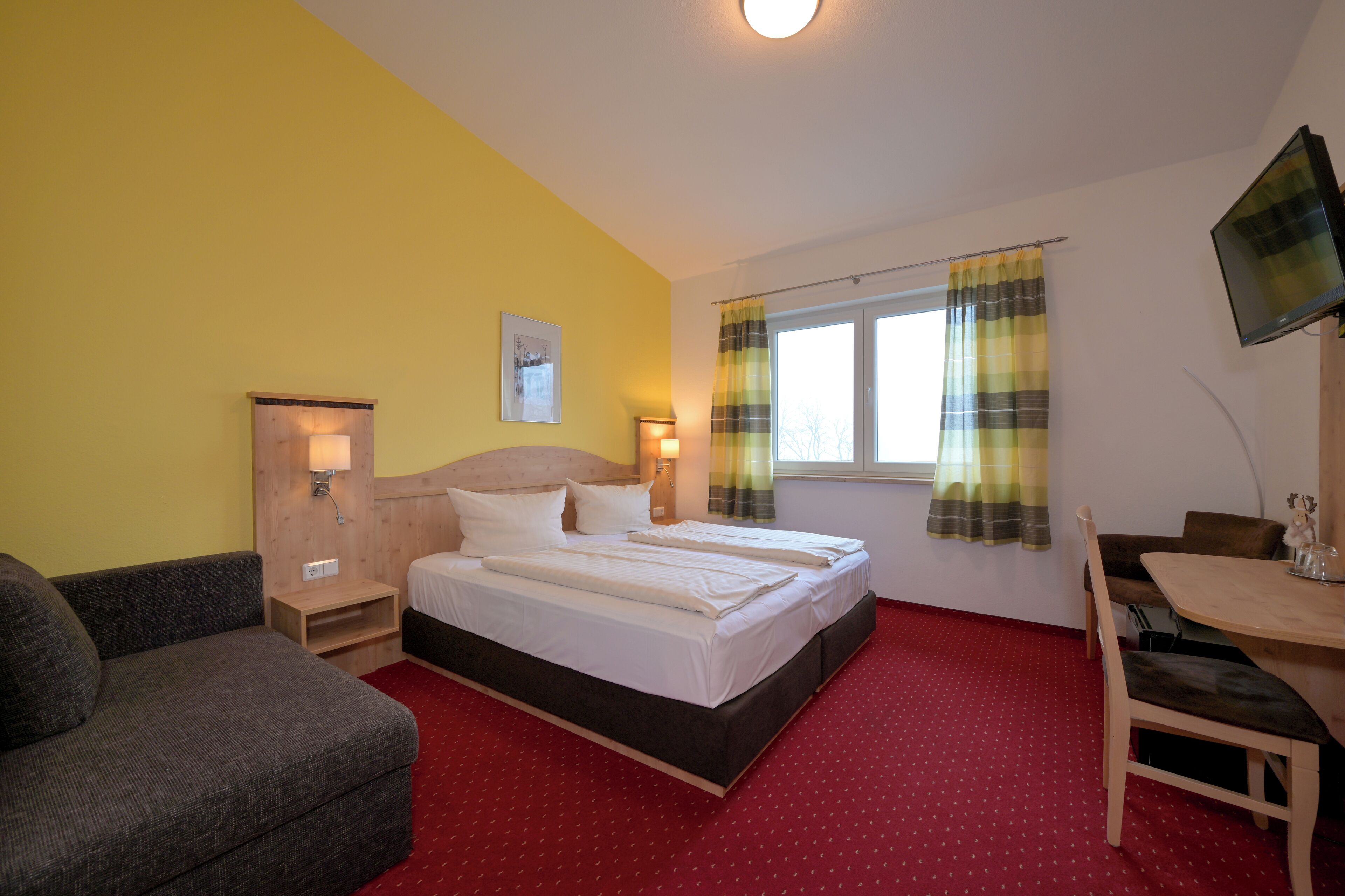 A hotel room with a bed, a sofa, a desk, and a TV.