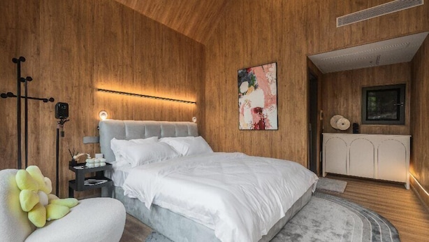 Un dormitorio moderno con una cama grande, paredes de madera, una mesita de noche con una lámpara y un cojín decorativo.