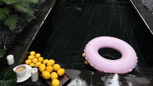 Una pequeña piscina rectangular al aire libre con suelo de baldosas negras, rodeada de abundante follaje y bambú.