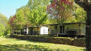 Fileira de casas móveis com área de estar externa, cercada por árvores e uma parede de pedra.