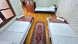 A room with two single beds, a wooden door, patterned wallpaper, and a red carpet.